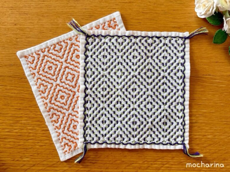刺し子ふきん「柿の花」の完成写真。紫とオレンジ色の2枚のふきんが並ぶ様子。