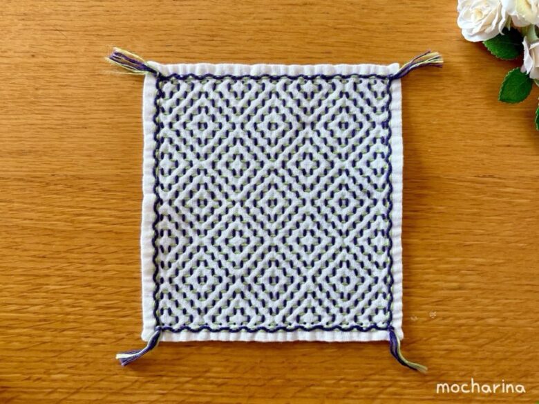 柿の花の刺し子ふきんの写真。額縁飾りと房を付けた様子。