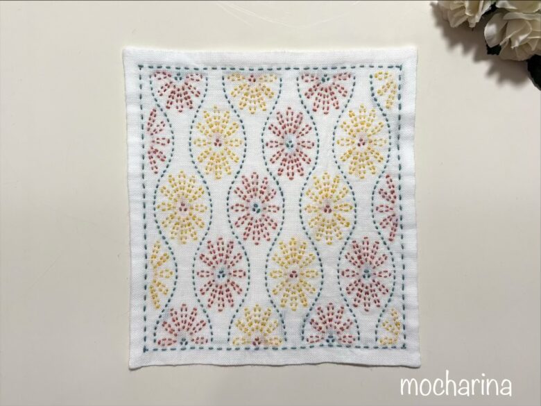 雲立涌文様の刺し子ふきんの完成写真。青緑色の波模様の間にオレンジと黄色の花柄が並んでいるデザイン。