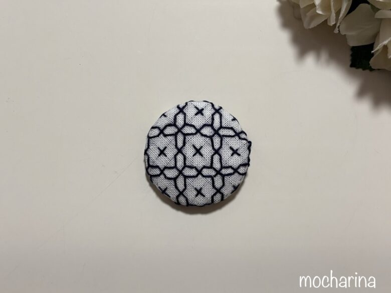 紺糸で作った十字花刺しの包みボタンの写真。